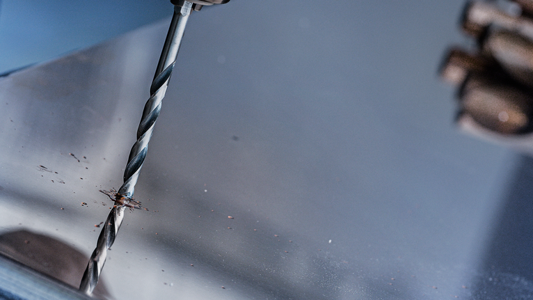 คนกำลังเจาะแผ่นโลหะ สวมอุปกรณ์ป้องกันความปลอดภัย