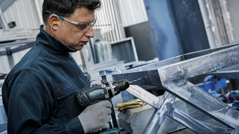 บุคคลที่สวมอุปกรณ์ความปลอดภัยกำลังเจาะเข้าไปในกรอบโลหะ