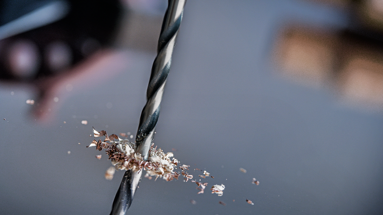 ดอกสว่านเจาะรูบนโลหะโดยมีเศษโลหะกระจัดกระจายอยู่ทั่วไป