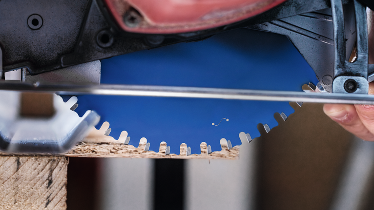 ผู้ที่กำลังใช้เลื่อยวงเดือนตัดไม้โดยดูภาพใบเลื่อยแบบใกล้ๆ