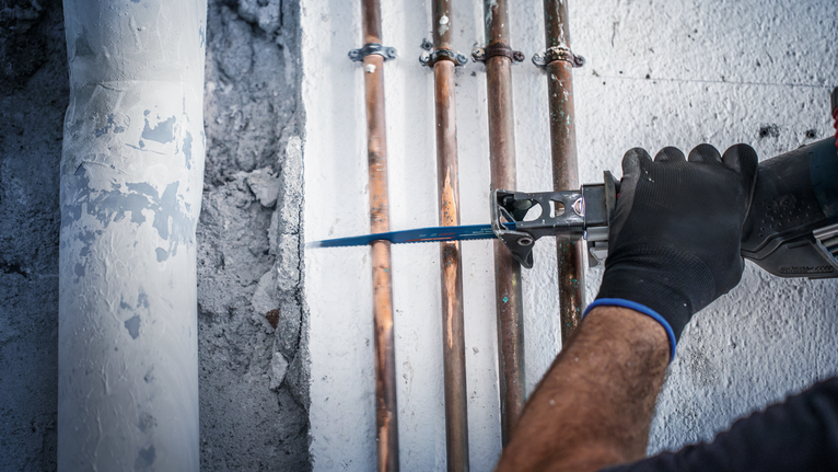 บุคคลที่สวมอุปกรณ์ความปลอดภัยกำลังใช้เลื่อยไฟฟ้าตัดท่อบนผนังคอนกรีต