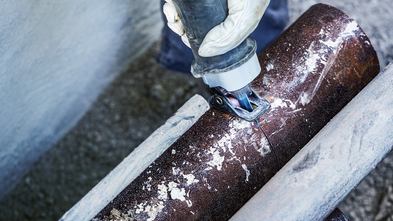 บุคคลที่สวมอุปกรณ์ความปลอดภัยใช้เครื่องมือไฟฟ้าตัดท่อโลหะ