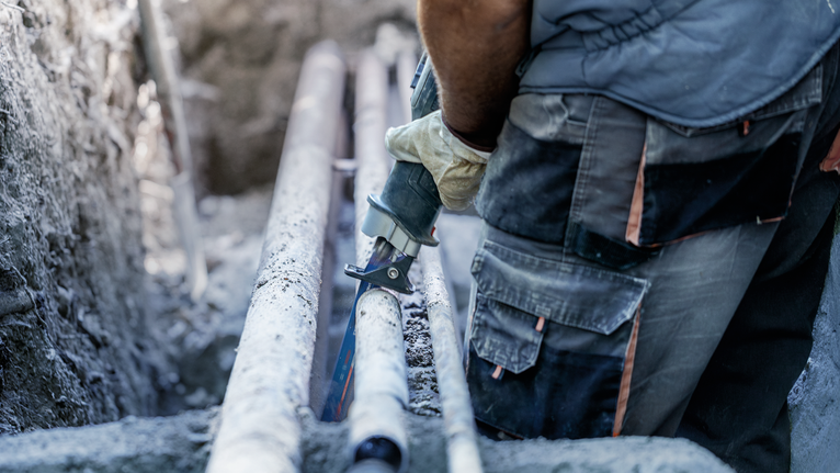 บุคคลที่สวมอุปกรณ์ความปลอดภัยกำลังใช้เลื่อยไฟฟ้าแบบลูกสูบตัดท่อ