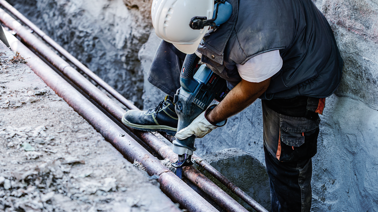 บุคคลที่สวมอุปกรณ์ความปลอดภัยกำลังเจาะท่อในสถานที่ก่อสร้าง