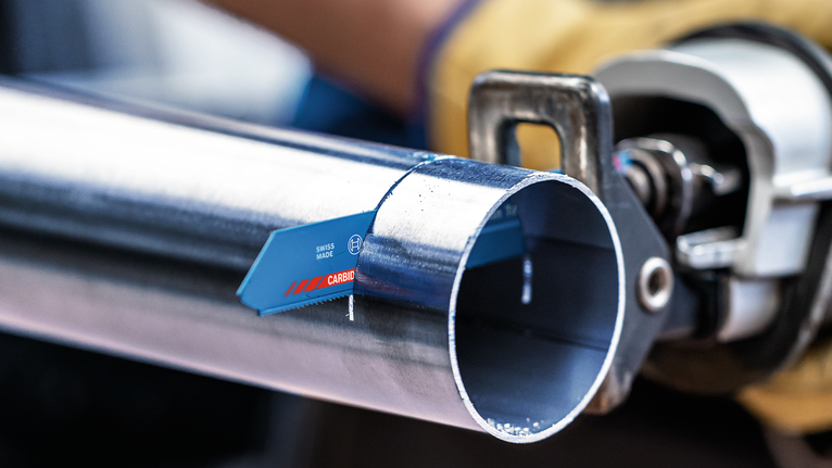 บุคคลที่สวมอุปกรณ์ความปลอดภัยกำลังตัดท่อโลหะด้วยเลื่อยไฟฟ้าแบบลูกสูบ