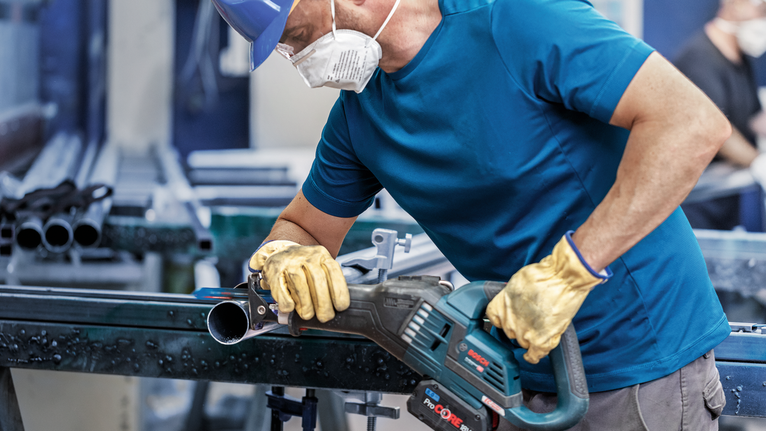 บุคคลที่สวมอุปกรณ์ป้องกันความปลอดภัยกำลังตัดท่อโลหะด้วยเครื่องมือไฟฟ้า