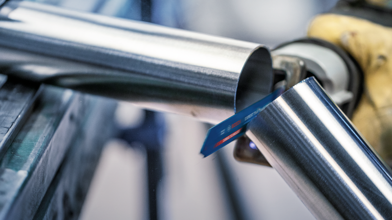 บุคคลที่สวมอุปกรณ์ความปลอดภัยกำลังตัดท่อโลหะด้วยเลื่อยไฟฟ้าแบบลูกสูบ