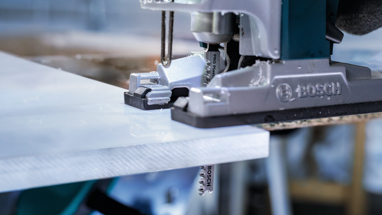 เลื่อยจิ๊กซอว์กำลังตัดแผ่นพลาสติกสีขาวในโรงงาน