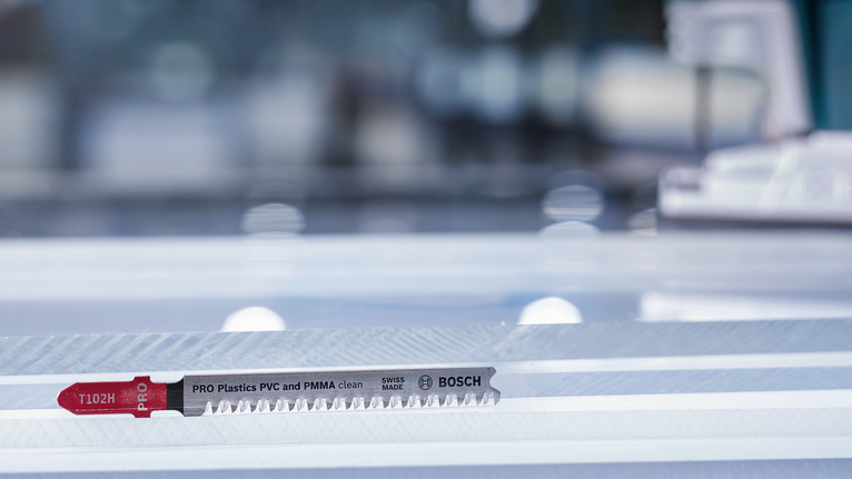 ใบเลื่อยจิ๊กซอว์สำหรับตัดพลาสติกวางอยู่บนพื้นผิวทำงานที่มีลายเส้น