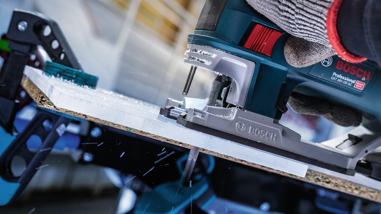 บุคคลที่สวมอุปกรณ์ความปลอดภัยกำลังใช้เลื่อยจิ๊กซอว์ตัดแผ่นวัสดุ