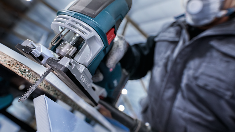 บุคคลที่สวมอุปกรณ์ความปลอดภัยกำลังใช้เลื่อยจิ๊กซอว์ตัดแผ่นวัสดุ