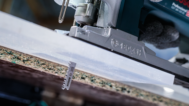 บุคคลที่สวมอุปกรณ์ความปลอดภัยกำลังใช้เลื่อยจิ๊กซอว์ตัดแผ่นไม้ลามิเนต