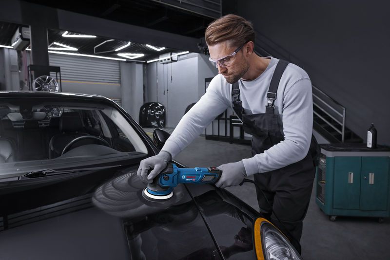 ชายคนหนึ่งสวมอุปกรณ์ป้องกันความปลอดภัย กำลังขัดฝากระโปรงรถสีดำด้วยเครื่องขัดเงาไฟฟ้า