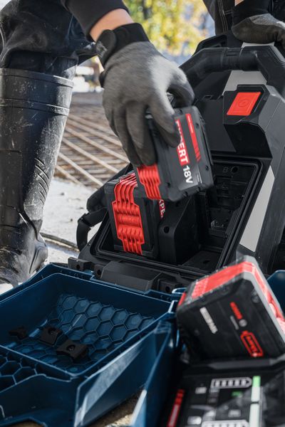 บุคคลที่สวมอุปกรณ์ความปลอดภัยกำลังใส่แบตเตอรี่ GPU18V2DI ขนาด 18 โวลต์ลงในแท่นชาร์จ