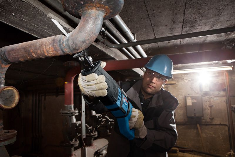 บุคคลที่สวมอุปกรณ์ความปลอดภัยกำลังตัดท่อโลหะด้วยเลื่อยตัดโลหะแบบลูกสูบ.