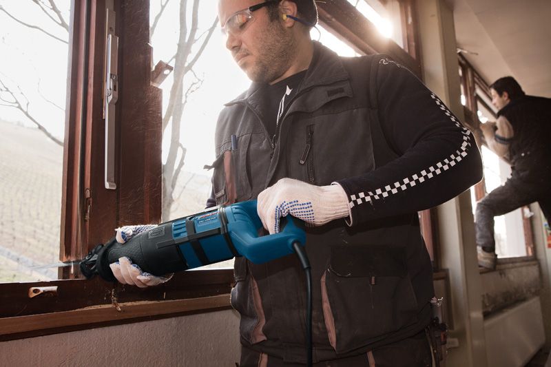 บุคคลที่สวมอุปกรณ์ด้านความปลอดภัยใช้เลื่อยตัดกรอบหน้าต่าง.