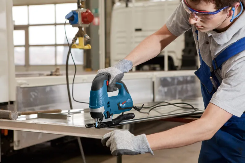 ผู้ที่สวมอุปกรณ์ด้านความปลอดภัยใช้เลื่อยจิ๊กซอว์ตัดแผ่นโลหะ.