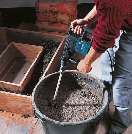 คนงานกำลังผสมปูนซีเมนต์ในถังโดยใช้เครื่องผสมสว่านไฟฟ้า.